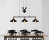 A black pendant light fixture with three lamps hangs above a wooden dining table with chairs. Anteprima dell’immagine prodotto