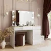 A modern white vanity table with a lighted mirror, makeup accessories, and a stool, set in a well-decorated room. Produktbild-Vorschau