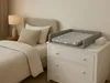 A nursery or bedroom setting with a changing station on top of a dresser next to a bed. Produktbild-Vorschau