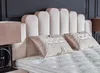 A close-up view of a bed with a tufted mattress and a padded headboard, featuring two decorative pillows. Produktbild-Vorschau
