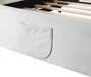 A close-up view of the side of a bed frame, showing a fabric pocket attached to the upholstered side. The wooden slats of the bed base are visible in the background. Produktbild-Vorschau