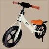 A white balance bike with orange accents and black wheels is shown against a plain light brown background. Náhled obrázku produktu