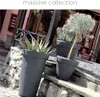 Three dark gray planters with plants are arranged on stone steps outside a building. Voir les images du produit