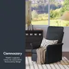 A dark gray recliner chair with a beige throw blanket and a white pillow with a black geometric pattern, placed in a living room setting with a window view of a garden and a lake. A black cabinet with books and cups is visible behind the chair. Podgląd zdjęcia produktu