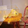 A string of decorative lights with spherical, filigree shades is draped over a table and a pink chair. Produktbild-Vorschau