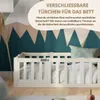 A white wooden bed gate with a lock, set against a wall with a mountain-like pattern. Produktbild-Vorschau