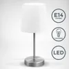 A white fabric table lamp with a silver base and stem, shown against a light gray and white gradient background. Icons indicating E14 socket, halogen, and LED compatibility are displayed to the right of the lamp. Podgląd zdjęcia produktu