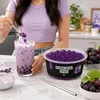 Frau in lila Top gibt Popping Boba Traube in ein Bubble-Tea-Glas Podgląd zdjęcia produktu