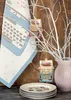 A festive Christmas display featuring a tea towel with a typewriter design, two typewriter ornaments hanging from white branches, and a stack of plates. Produktbild-Vorschau