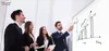 A group of business professionals are gathered around a whiteboard, with one person pointing to a growth chart drawn on it. Produktbild-Vorschau