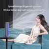 A woman is sitting on a couch next to a small fan, enjoying the cool air. Produktbild-Vorschau