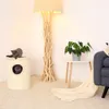 A cozy living room scene featuring a cat tree, a floor lamp, a small side table with a plant, and a sofa with a blanket. Produktbild-Vorschau