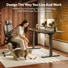 A woman is sitting in an office chair and playing with her cat in front of a standing desk with two monitors. Produktbild-Vorschau