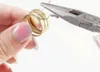 A person's hands are shown using pliers to manipulate a gold-colored ring with a small spring attached. Produktbild-Vorschau