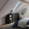 A bedroom with a slanted ceiling, featuring a dark cabinet with shelves and sliding doors, a bed with blue bedding and a white throw, and a skylight. Anteprima dell’immagine prodotto