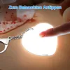 A finger is pressing a heart-shaped LED light keychain, which is illuminated. Produktbild-Vorschau
