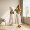 A woman is trying on an outfit in front of a full-length mirror in a well-lit room. Produktbild-Vorschau