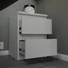A white bedside table with two drawers is shown in a room with gray walls and a gray tiled floor. An alarm clock is on top of the table. Anteprima dell’immagine prodotto