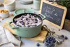 A green Staub pot filled with blueberry dessert, surrounded by blueberries and a small chalkboard with French text. Produktbild-Vorschau