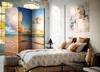 A bedroom with a bed, a room divider with a beach scene, and artwork on the wall. Produktbild-Vorschau