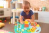A baby is playing with a colorful activity table in a room that appears to be a playroom or nursery. Podgląd zdjęcia produktu