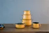 A set of orange pots and pans are arranged on a wooden table against a textured gray wall. Podgląd zdjęcia produktu