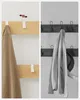 Collage showing two different angles of a wooden coat rack with hooks. The left side shows a close-up of two white hooks on a light wood panel, with a beige garment hanging on one hook and arrows indicating movement. The right side is in grayscale and show Náhled obrázku produktu
