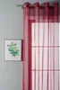 A close-up of a red sheer curtain hanging in front of a window, with a framed picture of a plant on the wall to the left. Produktbild-Vorschau