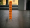 An orange ruler with markings from 30 to 100 is standing upright on a textured surface, possibly a floor. The background shows a blurred window and wall. Náhľad obrázku produktu