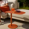 A person sitting on a couch next to an orange side table with a drink and sunglasses on it. Produktbild-Vorschau