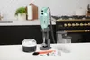 A Bamix immersion blender and its accessories are displayed on a kitchen counter in front of a stove. Náhled obrázku produktu