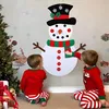 Two children in pajamas are interacting with a large felt snowman decoration on a wall, with a Christmas tree and gifts in the foreground. Náhľad obrázku produktu