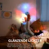 A child lying in bed playing with a flying spinner ball that projects colorful lights onto the wall. Produktbild-Vorschau