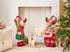Two plush reindeer decorations are displayed in a festive Christmas setting, with a Christmas tree and candles in the background. Náhľad obrázku produktu