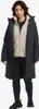 A woman wearing a black winter jacket over a beige fleece jacket and black leggings. Produktbild-Vorschau
