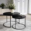 Two black round coffee tables are placed on a rug in a living room setting, with a vase of flowers on the larger table and a mug on the smaller table. A white cabinet with louvered doors is in the background. Anteprima dell’immagine prodotto