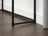 A close-up view of the black metal legs of a console table resting on a dark wood floor, with a white baseboard and wall in the background. Produktbild-Vorschau