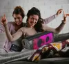 Two young women are dancing and listening to music on a portable speaker. Produktbild-Vorschau