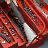 A hand is holding a vacuum cleaner attachment with white bristles, inserting it into a red metal toolbox filled with various tools and hardware. Produktbild-Vorschau