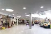 Interior view of a shopping mall with various storefronts and a produce stand. Produktbild-Vorschau