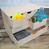 A wooden organizer box with multiple drawers filled with office supplies and personal items, placed on a wooden surface against a brick wall. Produktbild-Vorschau