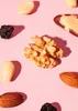 A collection of nuts and dried fruit scattered on a pink background. Produktbild-Vorschau