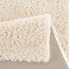 A close-up view of a cream-colored shaggy rug, showing its texture and the underside. Produktbild-Vorschau