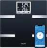 A black digital body analysis scale with a silver trim, shown with a smartphone displaying a health app. Produktbild-Vorschau