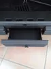 A close-up view of a black metal drawer with a small knob, part of a larger appliance, resting on a tiled floor. Náhled obrázku produktu