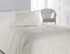 A bed with a pillow and a comforter, with a wicker chair in the background. Anteprima dell’immagine prodotto