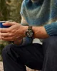 A person wearing a sweater and jeans, holding a blue mug and wearing a watch. Podgląd zdjęcia produktu
