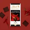A Lindt Excellence dark chocolate bar with chili, surrounded by red chili peppers and pieces of chocolate. Produktbild-Vorschau