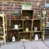 Wooden crates stacked against a brick wall, decorated with plants and gardening tools. Produktbild-Vorschau