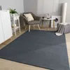 A dark gray rug is laid out on a light wooden floor in a modern living room setting. A gray armchair with a cream cushion sits on the rug, next to a small white side table with a plant and a decorative object. A white cabinet is visible on the left, and a  Produktbild-Vorschau